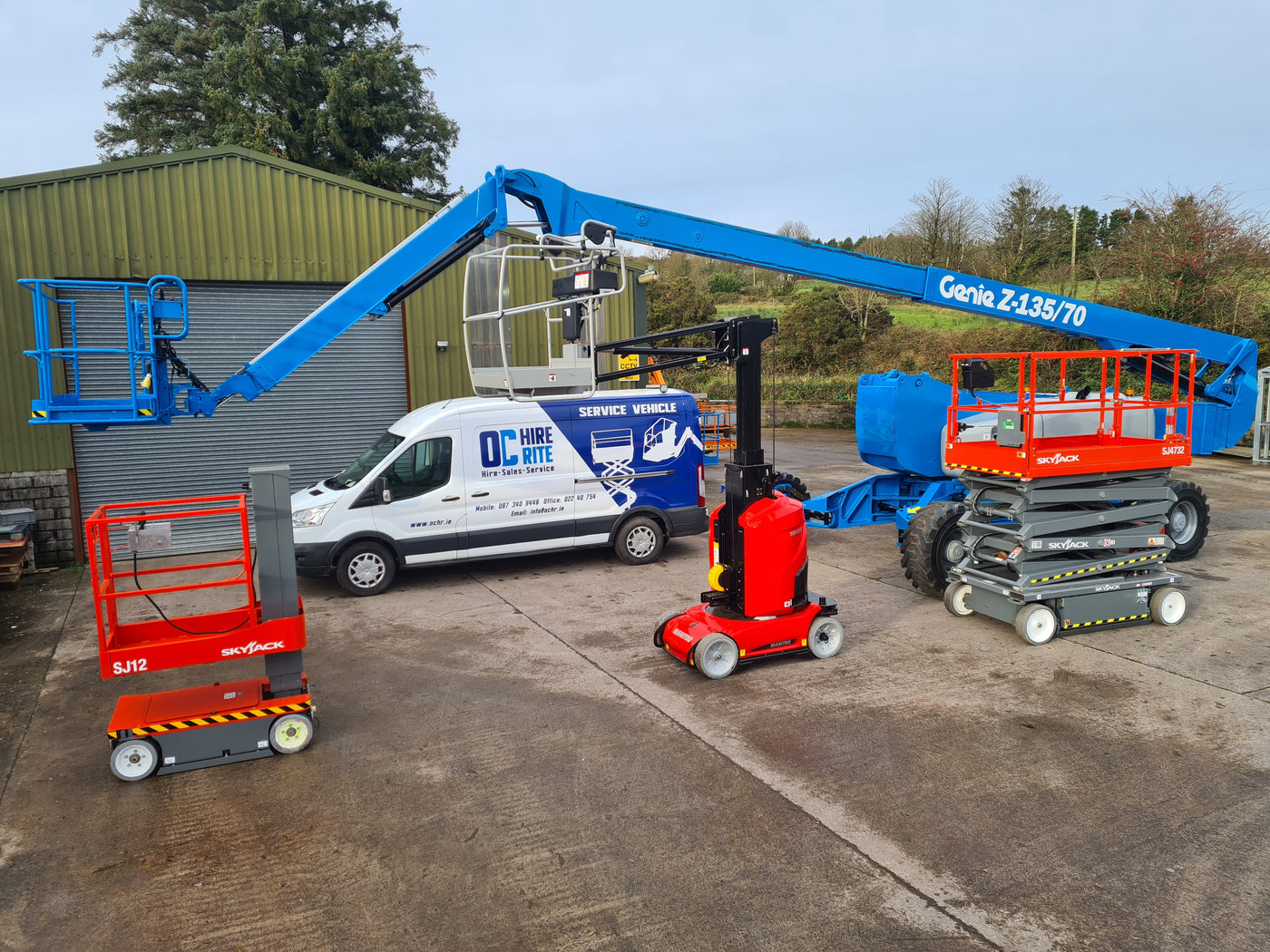 Three aerial lifts with a van in the background on a concrete surface.