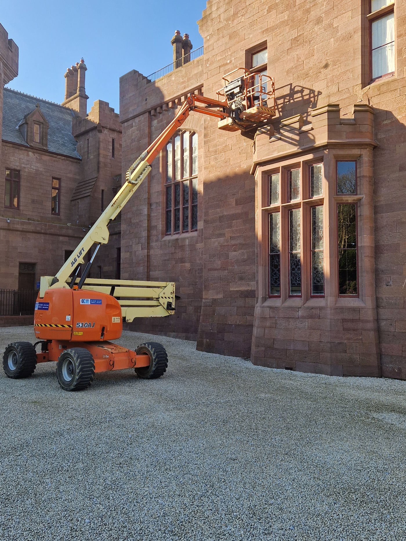 Orange cherry picker in front of a large stone building with arched windows.